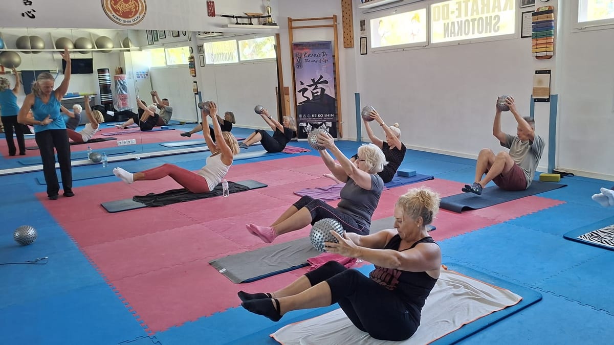 La instructora dirige la clase de pilates mientras el grupo trabaja el abdomen sosteniendo balones de masaje